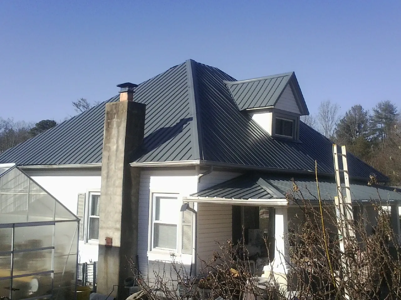 Dark blue standing seam metal roof on a white farmhouse with dormer — Slate & Tile Roof Repair by Roofing Brothers in Highlands