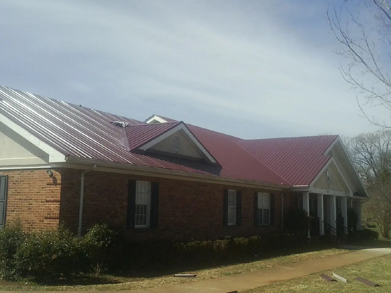 Red metal roof with gabled entries on a long brick building, from a Hail Damage Roof Repair job in Highlands