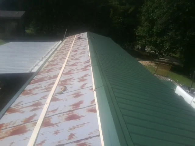 Old rusted panels beside newly installed green metal roofing — Wind Damage Roof Repair by Roofing Brothers in Highlands