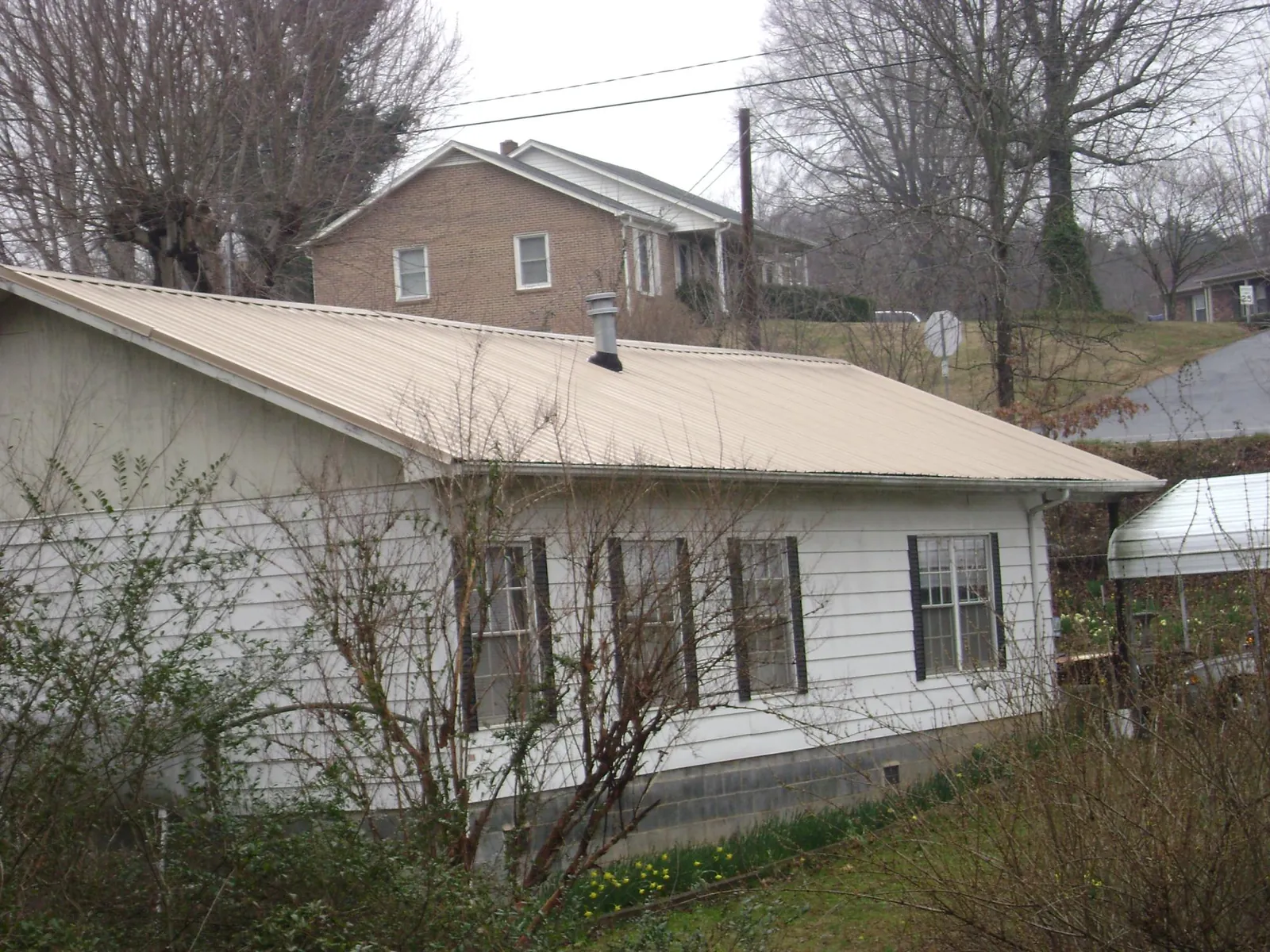 Tan metal roof on a white sided house set into a hillside — Commercial Roofing by Roofing Brothers in Highlands