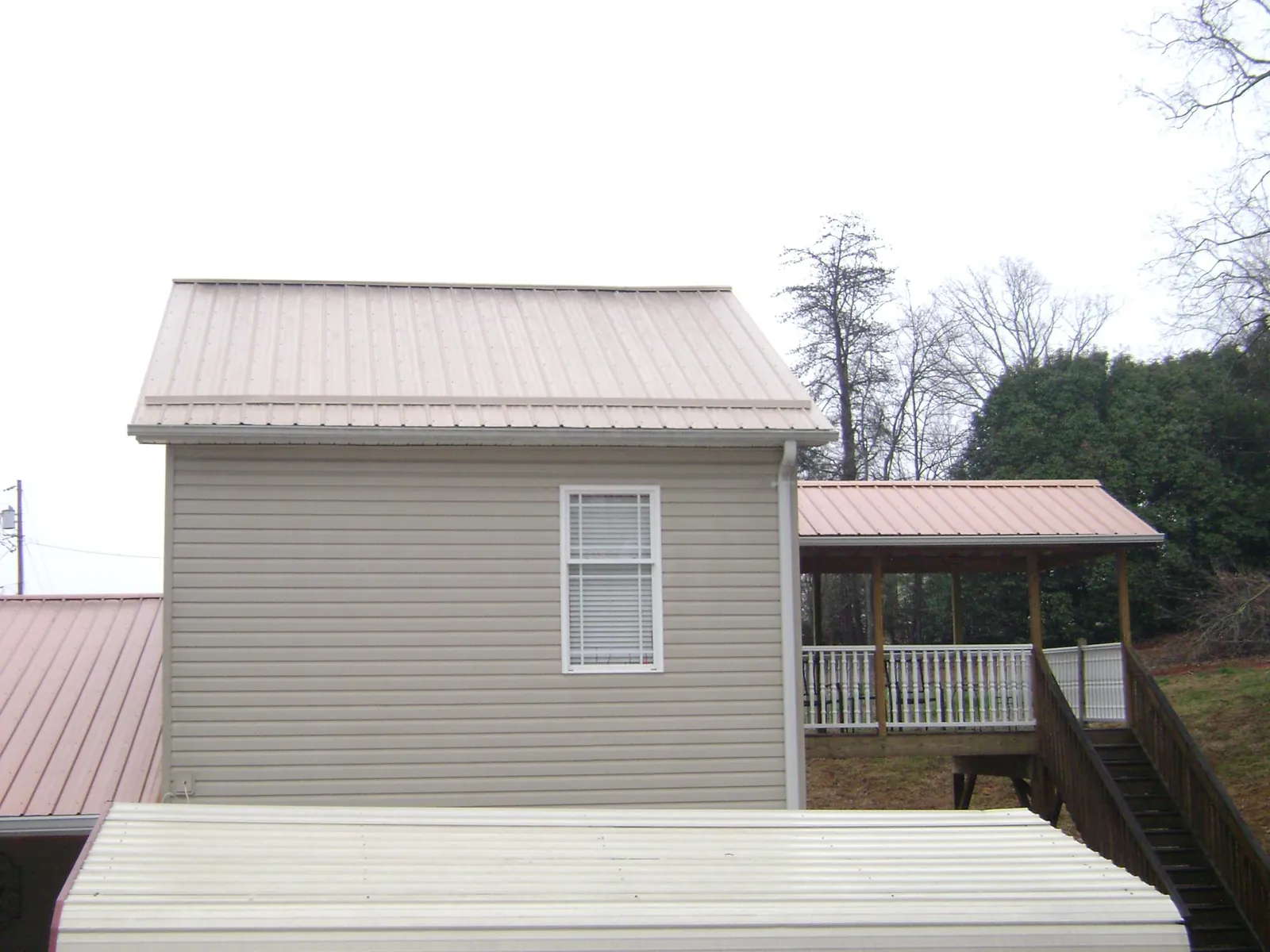 Tan metal roofs on a two story addition and attached porch, from a Roof Replacement job in Highlands