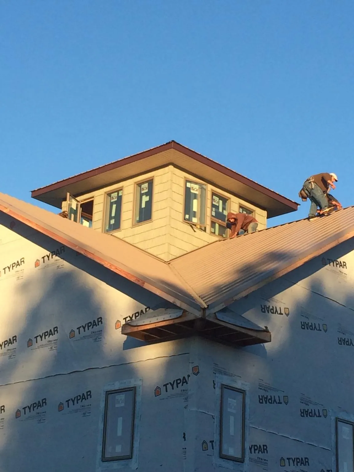 Roofers working around a rooftop cupola on a new metal roof at sunset — Roof Waterproofing in Highlands by Roofing Brothers